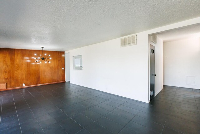 unfurnished room with a notable chandelier, dark tile patterned flooring, a textured ceiling, and wood walls