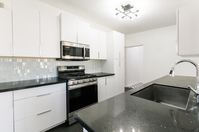 kitchen with sink, appliances with stainless steel finishes, dark stone countertops, backsplash, and white cabinets