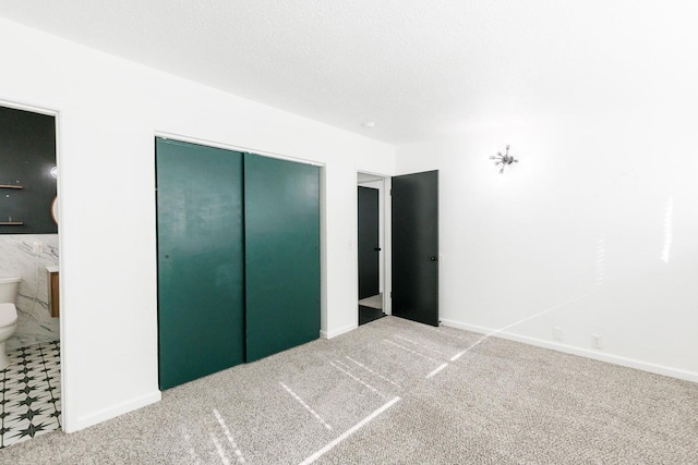 unfurnished bedroom with ensuite bath, carpet floors, a closet, and a textured ceiling