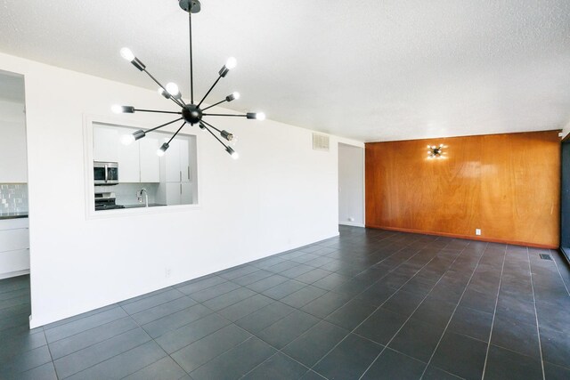 unfurnished living room with sink, wood walls, an inviting chandelier, a textured ceiling, and dark tile patterned flooring