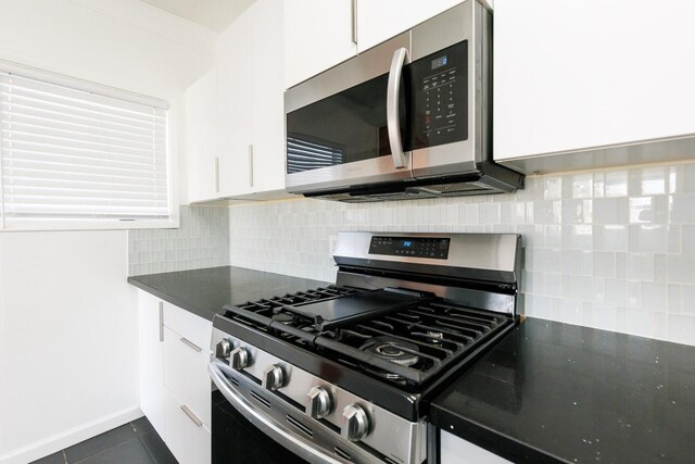 kitchen with backsplash, stainless steel appliances, dark tile patterned floors, and white cabinets