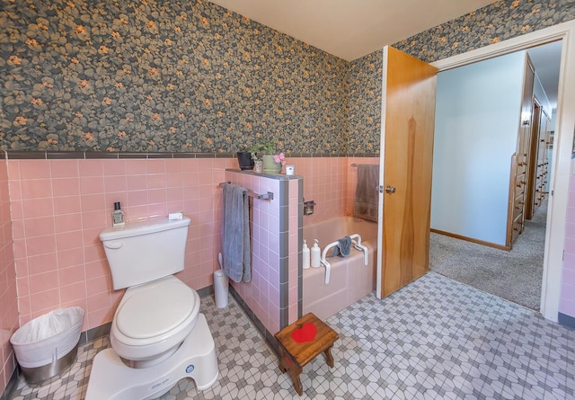 full bath with wainscoting, toilet, tile walls, wallpapered walls, and a bath