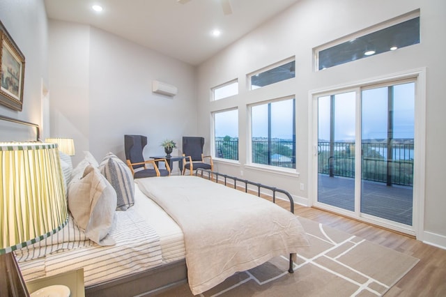 bedroom featuring a wall mounted AC, hardwood / wood-style flooring, a high ceiling, access to outside, and ceiling fan