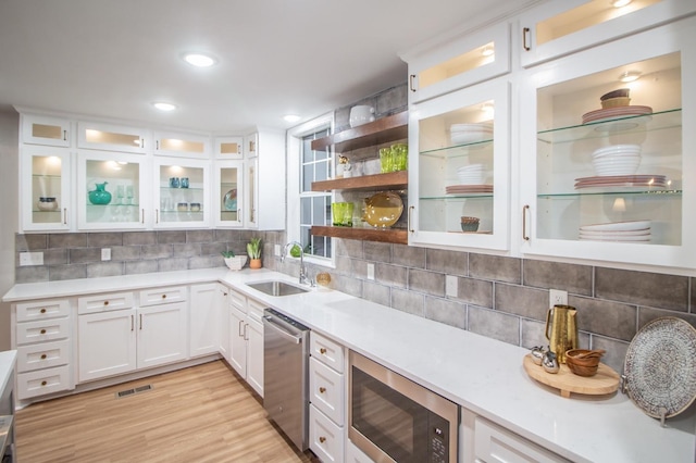 kitchen with black microwave, dishwasher, sink, white cabinets, and light wood-type flooring