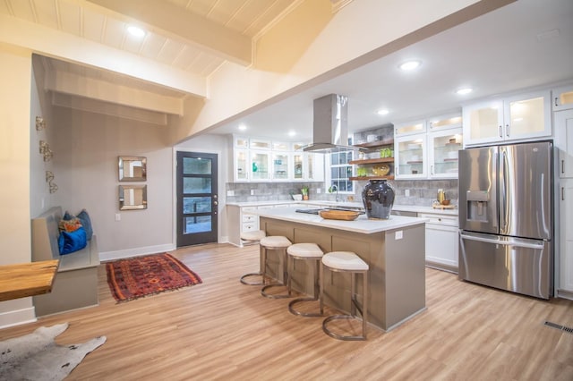 kitchen featuring white cabinetry, stainless steel fridge, a kitchen breakfast bar, island exhaust hood, and a center island