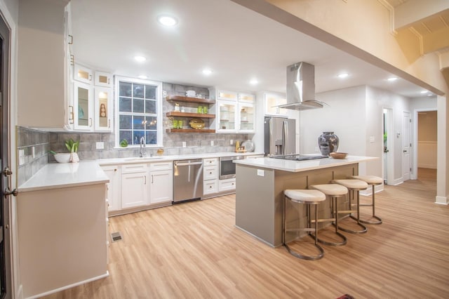 kitchen with a kitchen island, white cabinetry, a kitchen bar, island exhaust hood, and stainless steel appliances