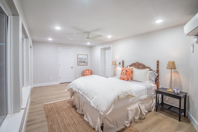 bedroom with a wall mounted air conditioner, light hardwood / wood-style floors, and ceiling fan