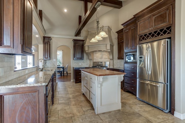 kitchen with sink, butcher block counters, stainless steel appliances, custom range hood, and decorative backsplash