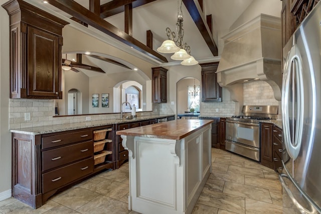 kitchen featuring butcher block countertops, decorative light fixtures, appliances with stainless steel finishes, custom range hood, and a kitchen island