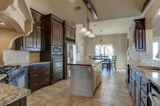 kitchen featuring sink, butcher block counters, stainless steel appliances, a center island, and decorative light fixtures