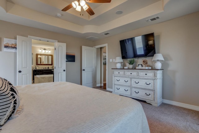 bedroom with a raised ceiling, ceiling fan, carpet floors, and ensuite bath