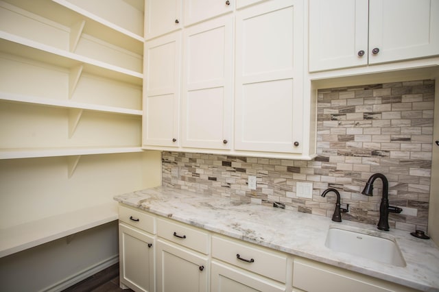 kitchen with decorative backsplash, light stone countertops, white cabinetry, open shelves, and a sink