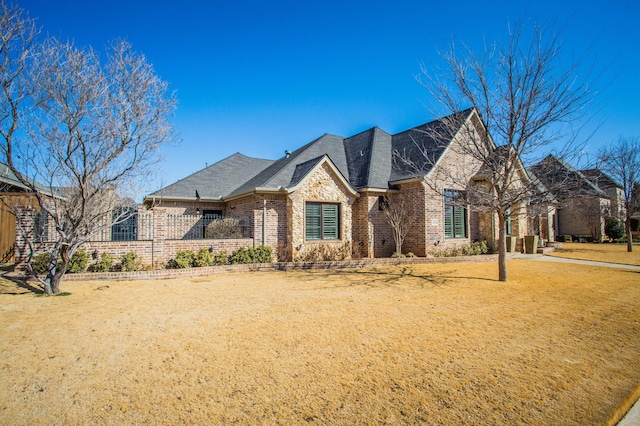 french provincial home with brick siding, fence, and a front lawn