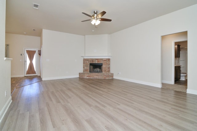 unfurnished living room with ceiling fan, a brick fireplace, and light hardwood / wood-style flooring