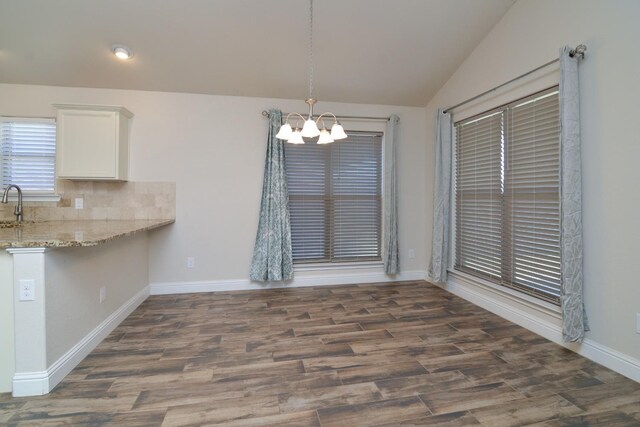 unfurnished dining area featuring an inviting chandelier, sink, dark wood-type flooring, and vaulted ceiling