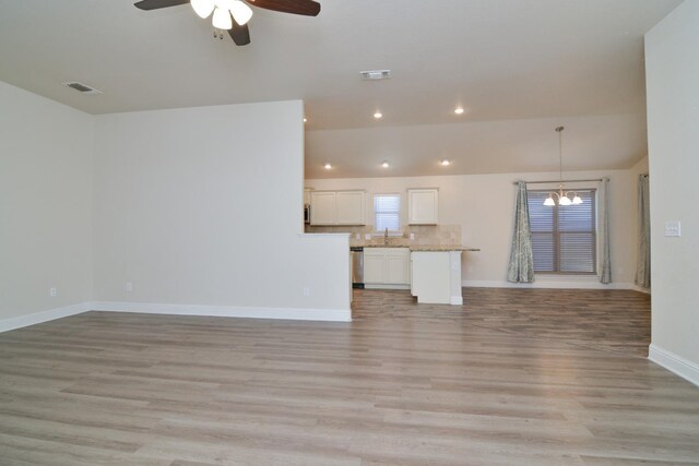 unfurnished living room featuring ceiling fan with notable chandelier and light hardwood / wood-style flooring