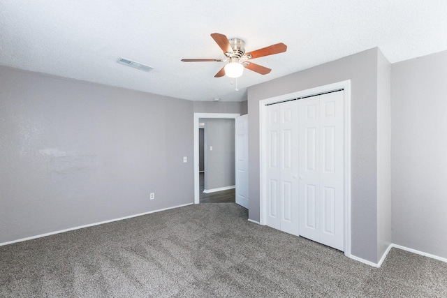 unfurnished bedroom with ceiling fan, a textured ceiling, dark carpet, and a closet