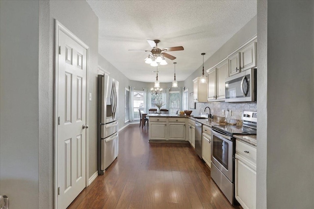 kitchen with sink, appliances with stainless steel finishes, dark hardwood / wood-style floors, decorative light fixtures, and kitchen peninsula