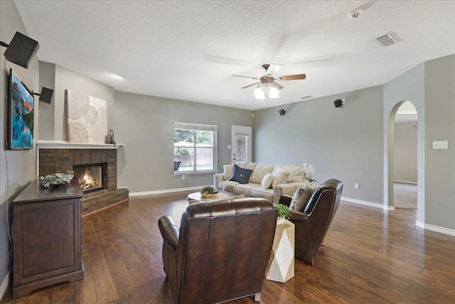 living room featuring ceiling fan, a fireplace, dark hardwood / wood-style floors, and a textured ceiling