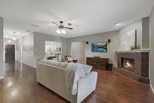 living room featuring ceiling fan, dark hardwood / wood-style floors, and a fireplace