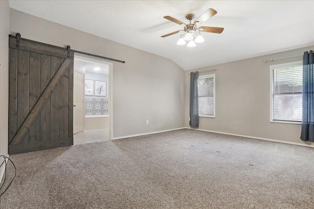 carpeted empty room featuring lofted ceiling, a textured ceiling, a barn door, and ceiling fan