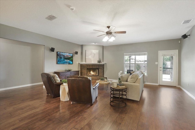 living room featuring a brick fireplace, dark wood-type flooring, a textured ceiling, and ceiling fan