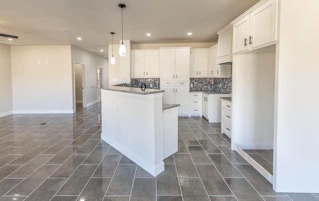 kitchen featuring white cabinetry, decorative light fixtures, a kitchen island, dark stone counters, and backsplash