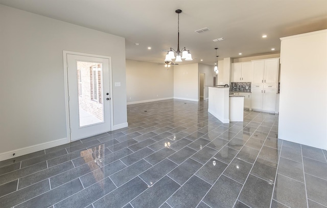 kitchen with ceiling fan with notable chandelier, hanging light fixtures, white cabinets, a kitchen island, and decorative backsplash