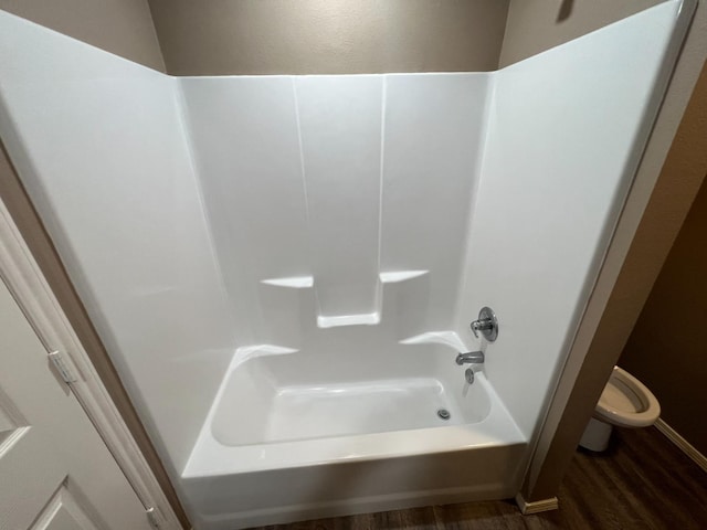 bathroom with hardwood / wood-style flooring, shower / bathtub combination, and toilet