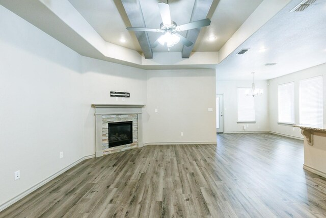 unfurnished living room with wood-type flooring, a stone fireplace, and ceiling fan with notable chandelier