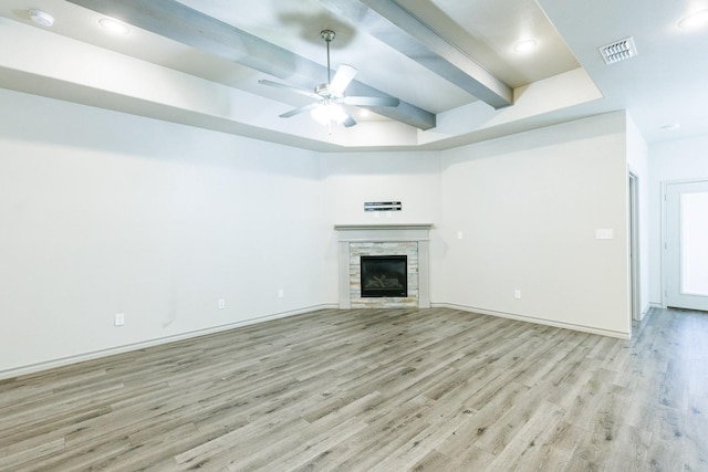 unfurnished living room featuring ceiling fan, a fireplace, a raised ceiling, and light hardwood / wood-style floors