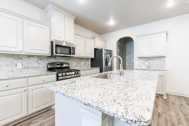 kitchen with sink, appliances with stainless steel finishes, light hardwood / wood-style floors, an island with sink, and white cabinets