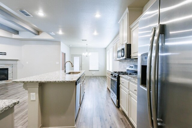 kitchen featuring sink, light stone counters, appliances with stainless steel finishes, a kitchen island with sink, and white cabinets