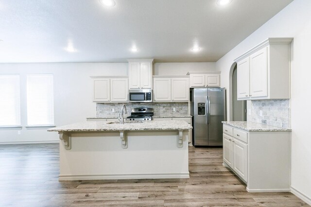 kitchen with appliances with stainless steel finishes, white cabinetry, sink, a kitchen bar, and light stone counters