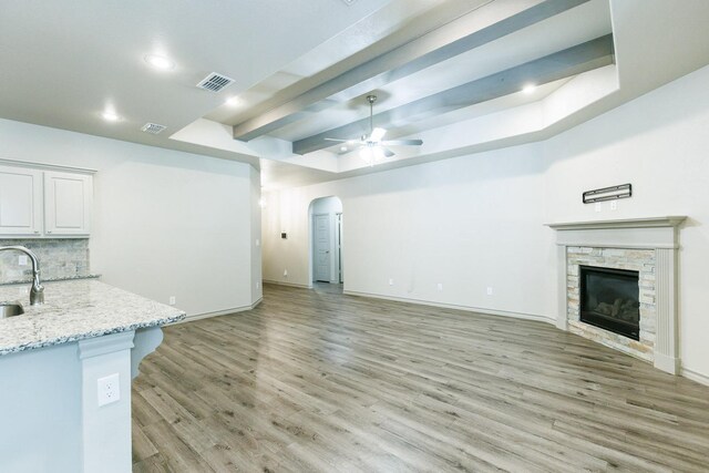 unfurnished living room with ceiling fan, a stone fireplace, sink, and light hardwood / wood-style flooring