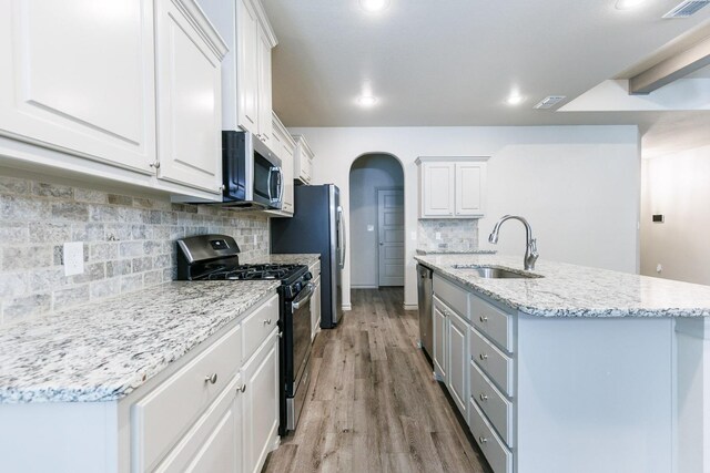 kitchen featuring sink, white cabinets, stainless steel appliances, light stone countertops, and light wood-type flooring