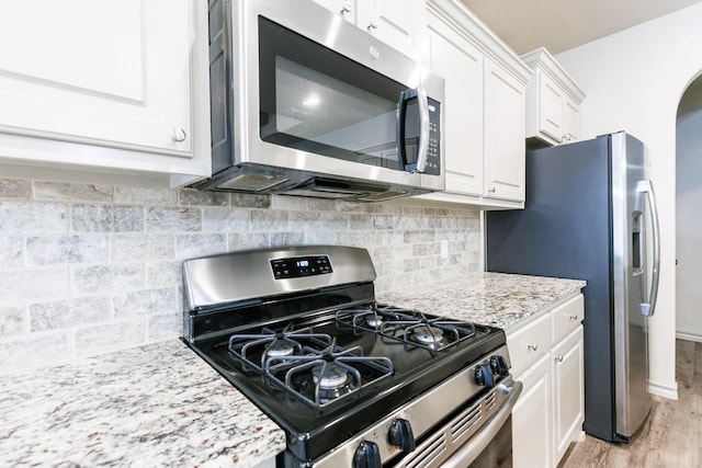 kitchen with light stone counters, appliances with stainless steel finishes, white cabinets, light hardwood / wood-style floors, and backsplash