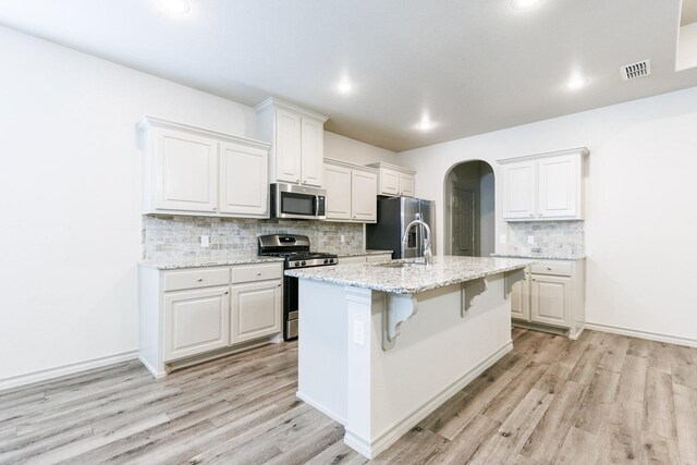 kitchen with white cabinetry, appliances with stainless steel finishes, a kitchen breakfast bar, and an island with sink