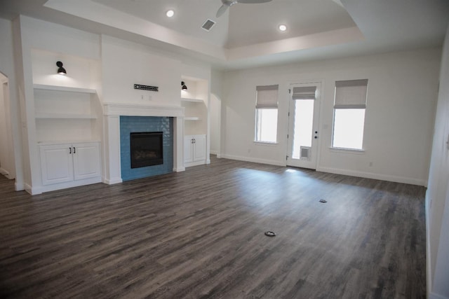 unfurnished living room with a raised ceiling, a tiled fireplace, dark wood-type flooring, and ceiling fan