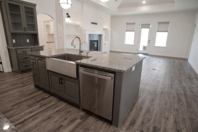 kitchen with sink, light stone counters, a center island with sink, stainless steel dishwasher, and a tile fireplace