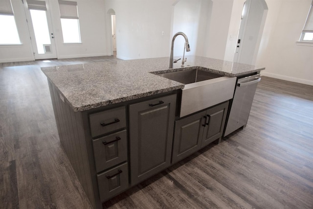 kitchen featuring dark wood-type flooring, sink, light stone counters, a center island with sink, and dishwasher