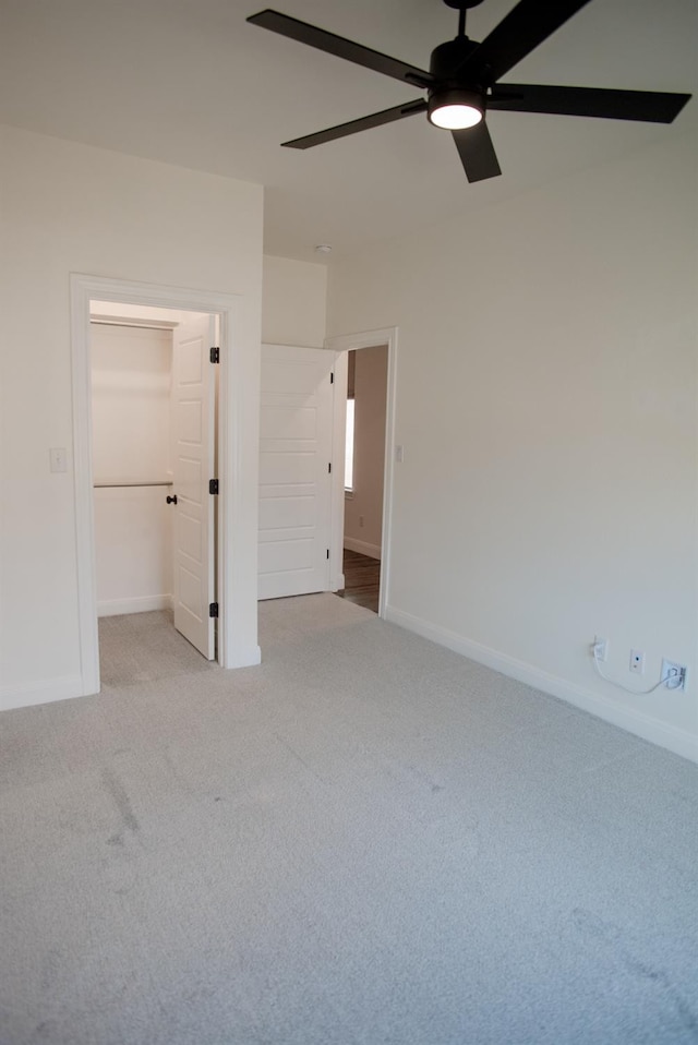 unfurnished bedroom with a walk in closet, light carpet, ceiling fan, and a closet