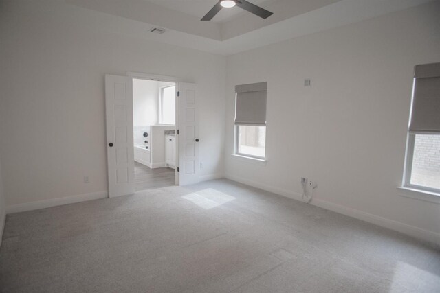 empty room featuring a raised ceiling, light carpet, and ceiling fan