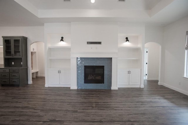 unfurnished living room featuring a tile fireplace, built in features, dark hardwood / wood-style flooring, and a tray ceiling