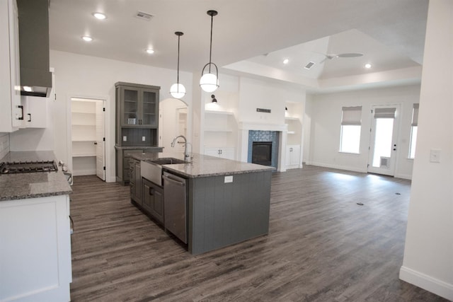 kitchen with decorative light fixtures, dishwasher, gray cabinetry, a raised ceiling, and a center island with sink