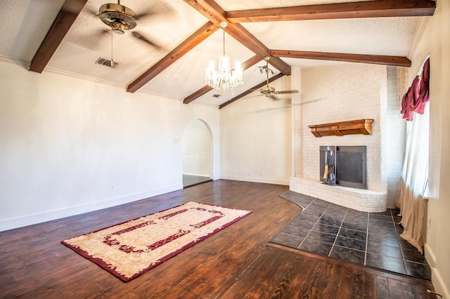 unfurnished living room with a brick fireplace, lofted ceiling with beams, ceiling fan with notable chandelier, arched walkways, and a textured ceiling