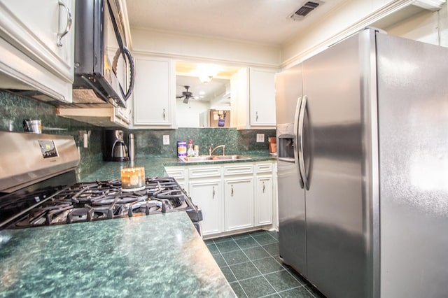 kitchen with dark tile patterned floors, a sink, tasteful backsplash, stainless steel appliances, and white cabinets