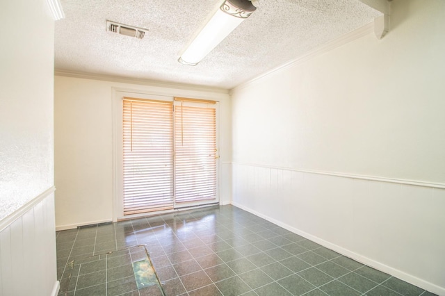 spare room featuring dark tile patterned flooring, visible vents, a wainscoted wall, and ornamental molding