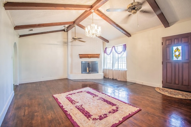 unfurnished living room with a brick fireplace, vaulted ceiling with beams, ceiling fan with notable chandelier, hardwood / wood-style flooring, and a textured ceiling