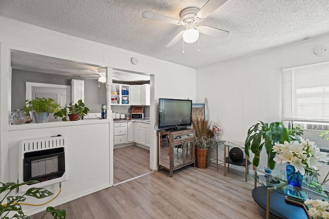 living room featuring ceiling fan, a textured ceiling, heating unit, and light wood-type flooring